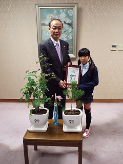 表彰状と副賞のクロマツとバラの苗木を大久保市長（左）から受け取る入間川さん