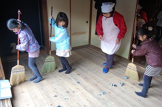 掃除機の代わりにぬれた新聞紙をまいて床を掃く子供たち