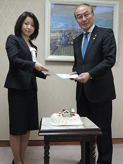 贈られたケーキの前に立つ横山社長（左）と大久保市長