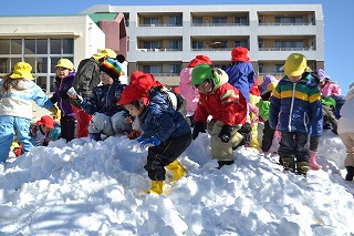園庭にできた雪山で元気に遊ぶ園児たち