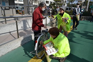  市役所前で自転車利用者に啓発リーフレットを渡し、反射板を取り付ける会員