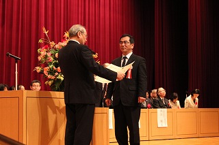  先月19日に東京都内で開かれた表彰式で表彰状を受け取る髙鍋校長（右） 